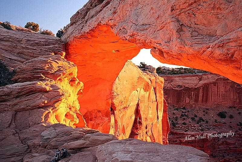 At a Mesa Arch sunrise in Canyonlands National Park, the sun glows orange and yellow on the underside of the sandstone arch.