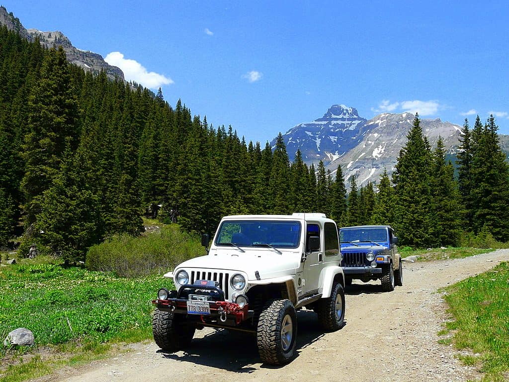 two jeeps on a dirt road with mountains in the distance