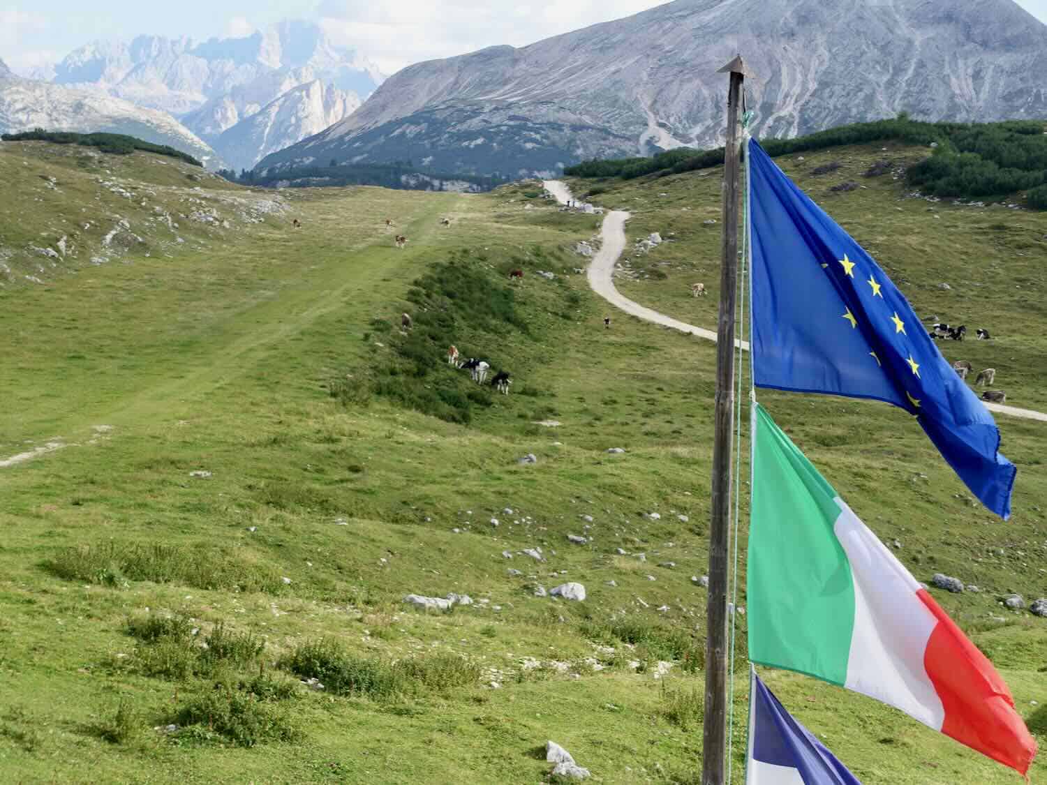 Flags on a flag pole overlooking a mountainous scenic view in the Dolomites of Italy.