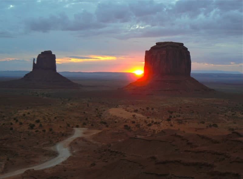 The sun rises behind east and west mittens in Monument Valley.
