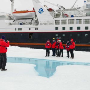 man taking photo of group standing on ice with cruise ship in background