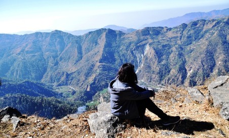Woman sitting on the ground looking at mountains.