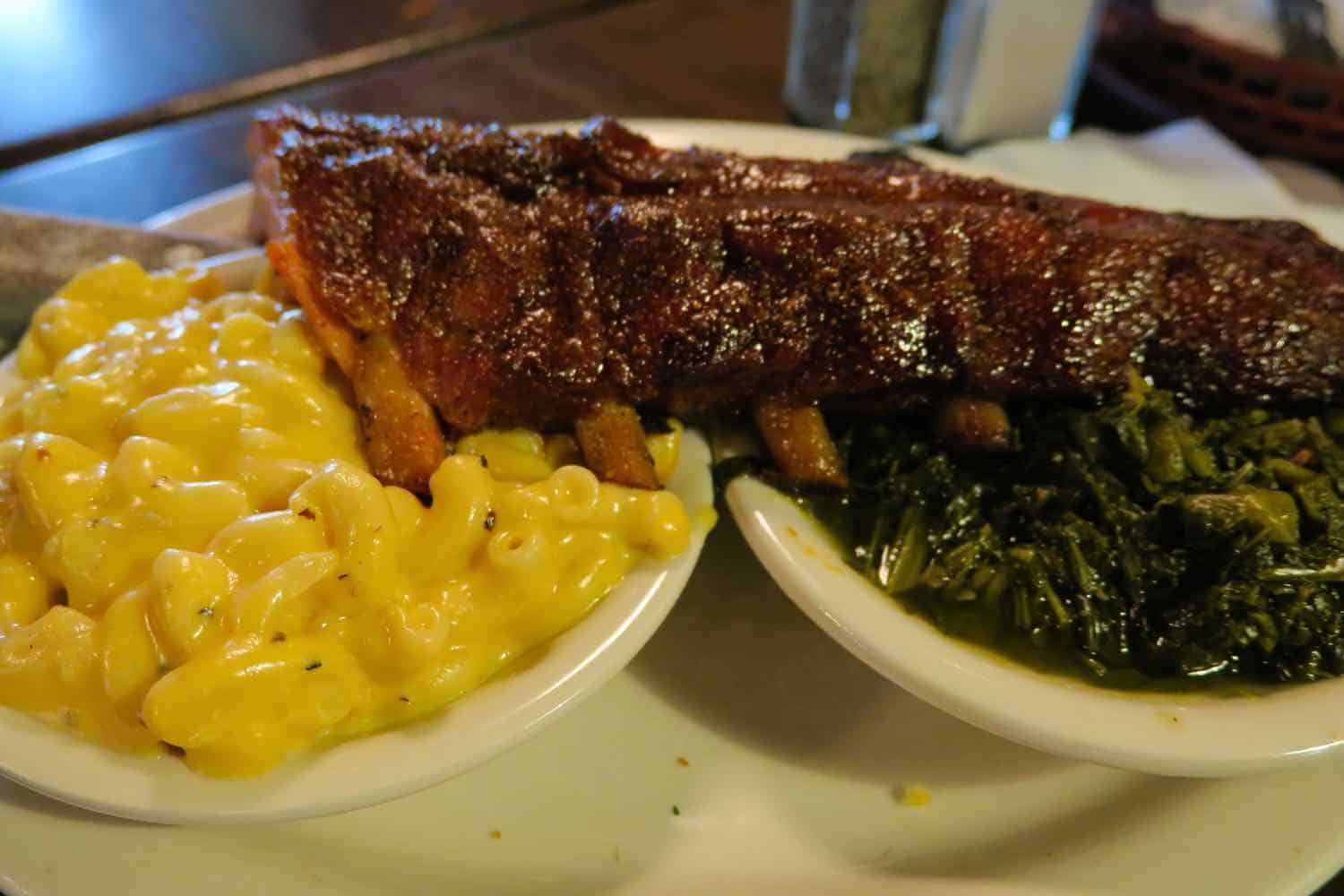 Barbecue ribs sitting on a small bowl of macaroni and cheese and a small bowl of turnip greens from Memphis Barbecue Company