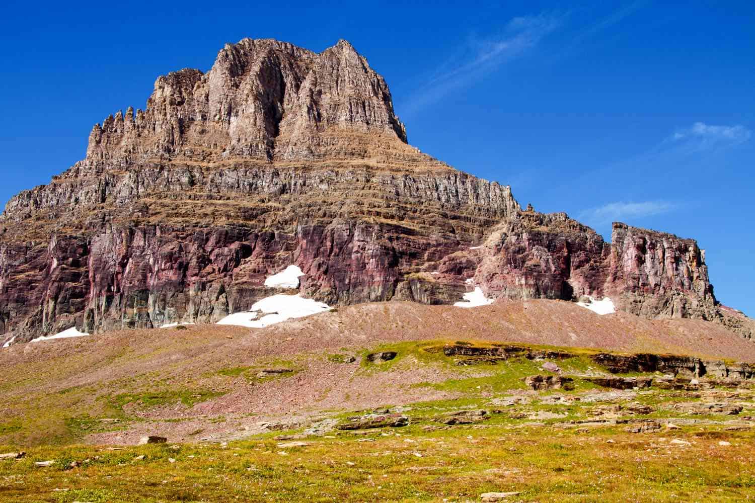 brown and gray mountain peak against a blue sky at the beginning of  Hidden Lake trail in Glacier National Park
