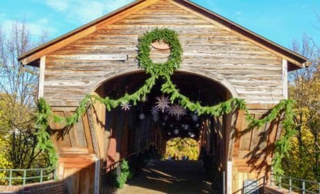 A brown covered bridge decorated with Christmas greenery