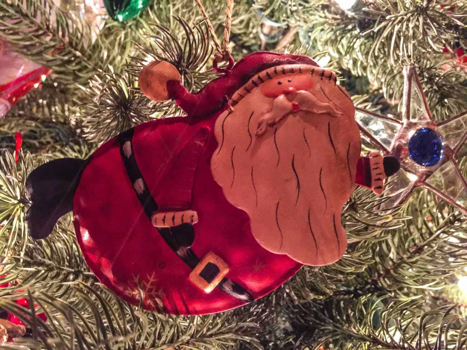 Red metal Santa ornament hanging on a Christmas tree.
