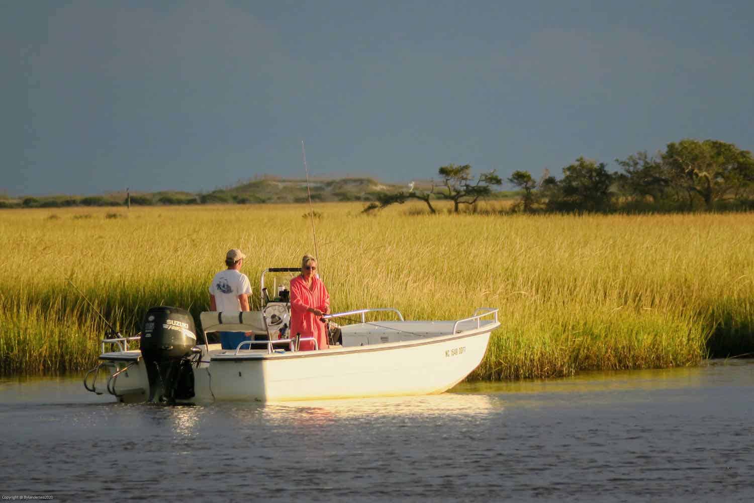 man and woman in a boat fishing with marshlands behind them in North Carolina.