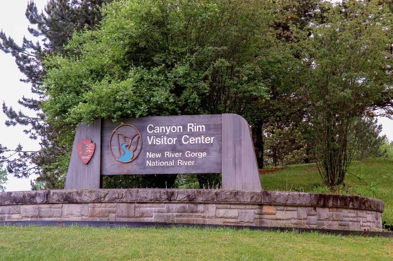 Wooden sign for Canyon Rim Visitor Center with trees in the background