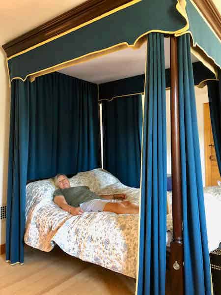 Colonial four poster bed surrounded by dark blue drapes and canopy.
