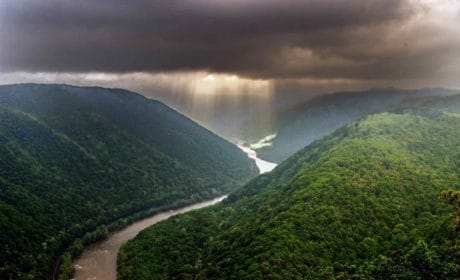 Light shafts stream through a storm cloud illuminating a river that flows between green mountains