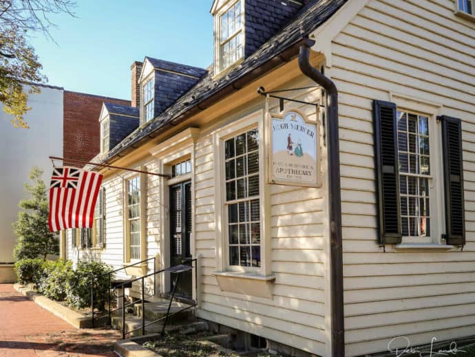 Cream colored clapboard house with black trim and colonial flag.