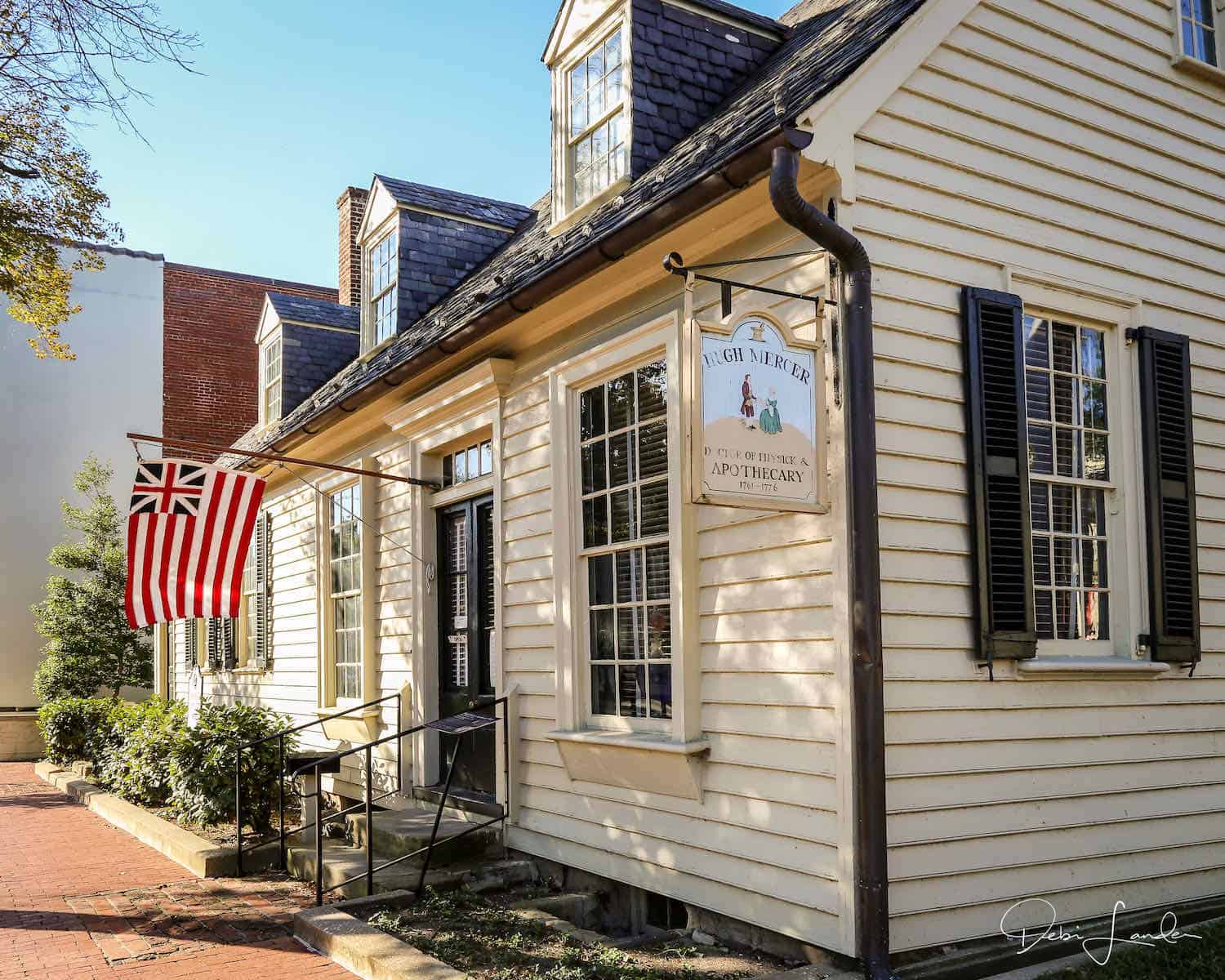 Cream colored clapboard house with black trim and colonial flag at Hugh Mercer Apothecary Shop in Fredericksburg, Va. 