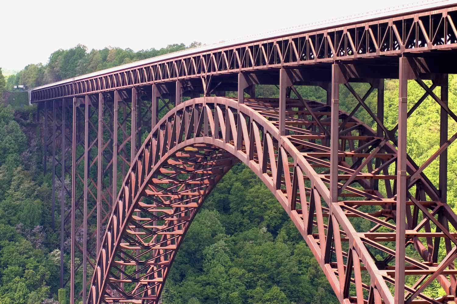 Red iron bridge that spans the New River Gorge with green trees in the background.