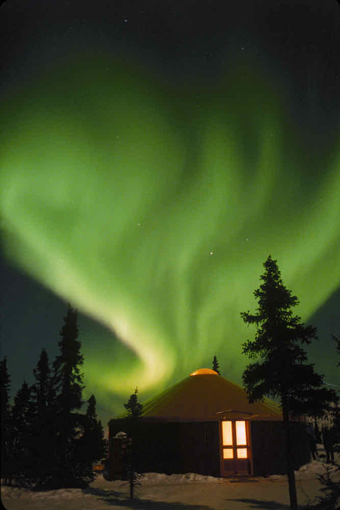 Green aurora borealis over a yurt in the winter