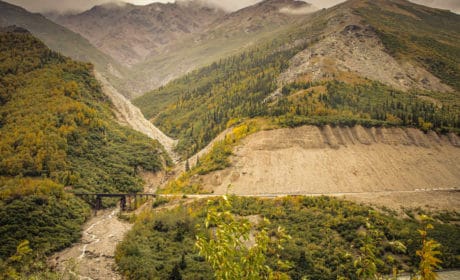rugged mountains with green trees, train trestle near bottom of phto