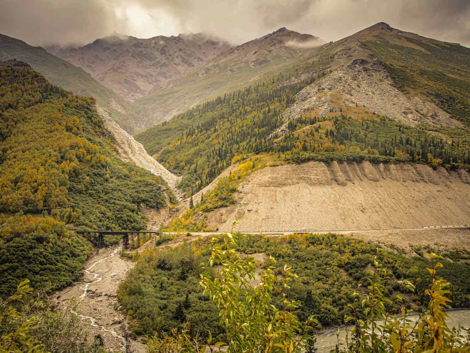 rugged mountains with green trees, train trestle near bottom of phto