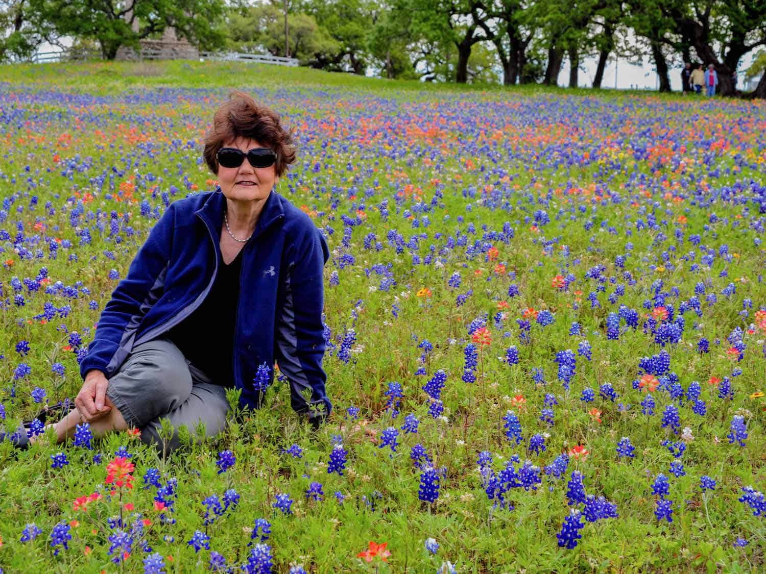 woman sitting in a field of blue and orange wildflowers