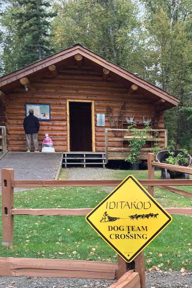log cabin in the woods with yellow Iditarod sign in front