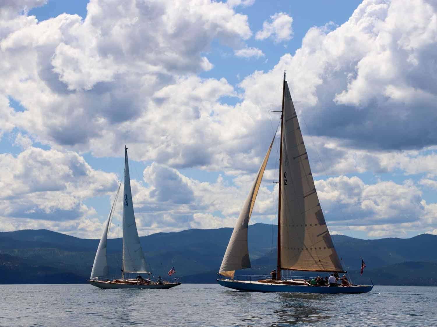 Two sailboats on Flathead Lake with mountains in the distance.