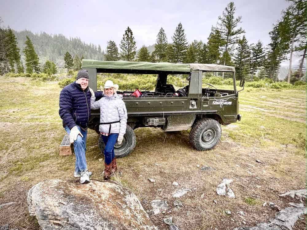 A man and woman pose in front of a vintage Pinzgauer at the Flathead Lake Lodge Elk Preserve.