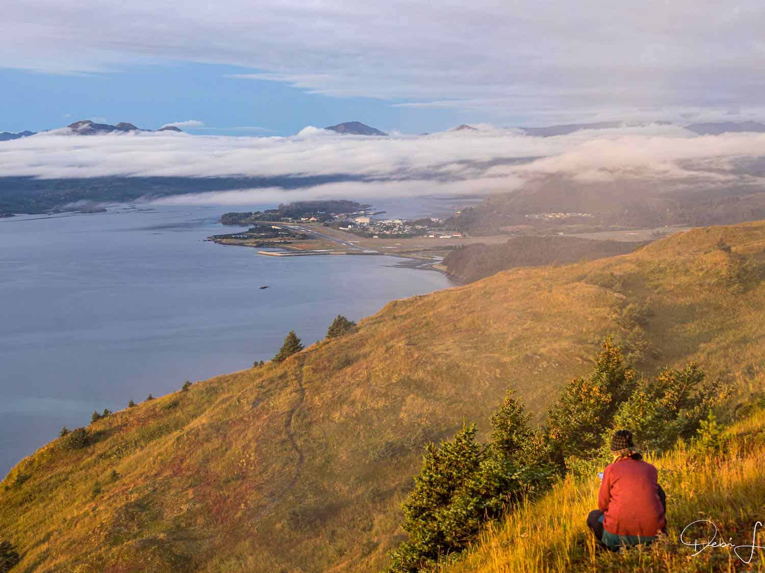 Woman sitting on the ground photographing the view at Pillar Mountain on Kodiak Island, Alaska