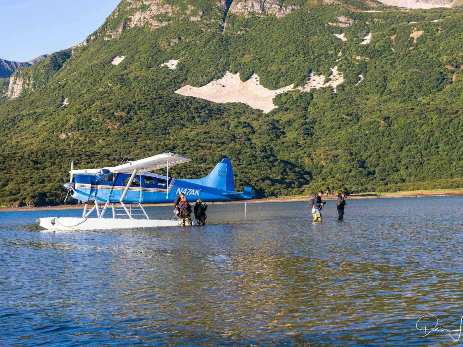 Float plane sitting on the water at Geographic Harbor in Katmai National Park with people walking to shore.