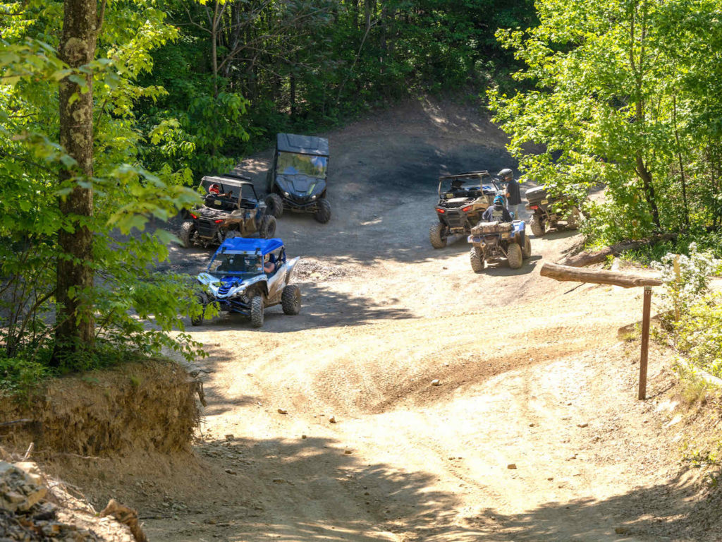 Group of ATV's parked on the side of a dirt trail.