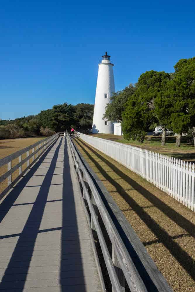 Gray wooden walkway leading up to a white lighthouse on Ocracoke Island, NC.