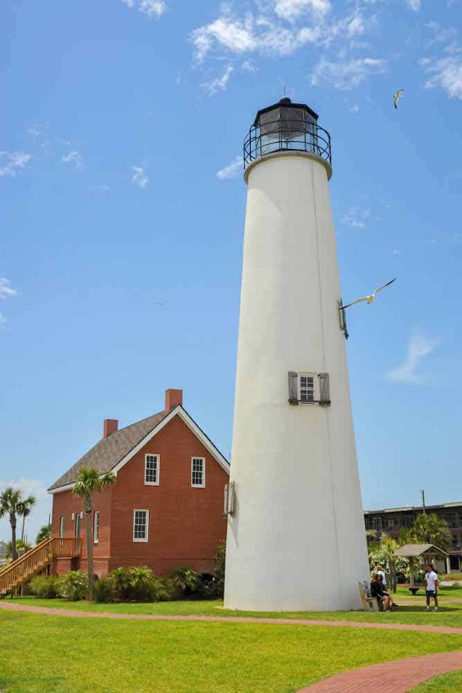 The white St. George Lighthouse stands tall next to a red brick building surrounded by lawn.