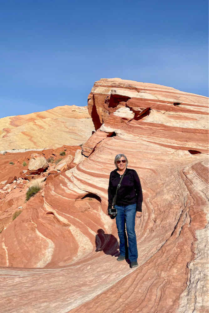 Boomer woman poses in front of undulating red rocks known as the Fire Wave in Valley of Fire State Park Nevada.