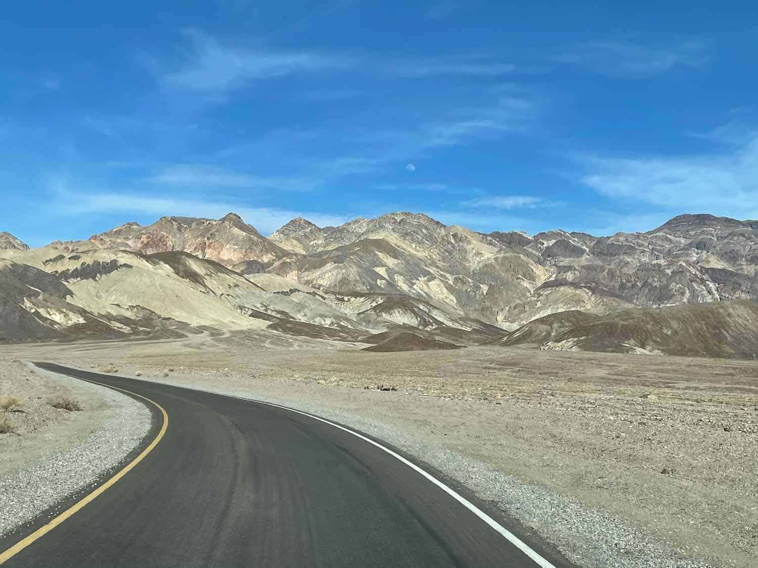 Paved road leading into the white and beige colored mountains of Death Valley National Park.