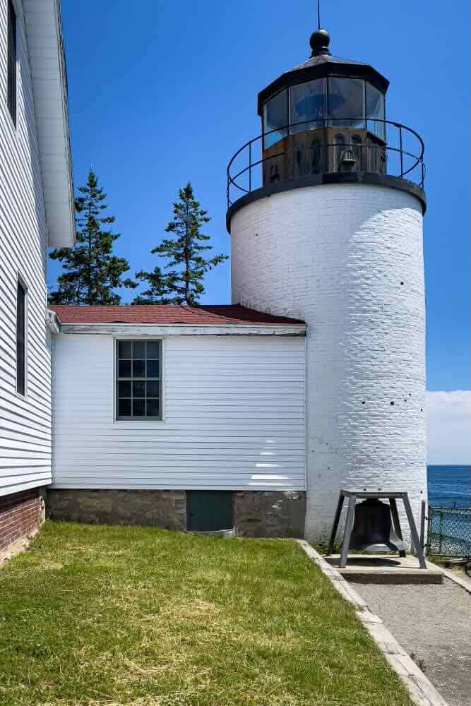 A white lighthouse (Bass Harbor Lighthouse) is attached to a white lightkeeper's house on the coast of Maine.