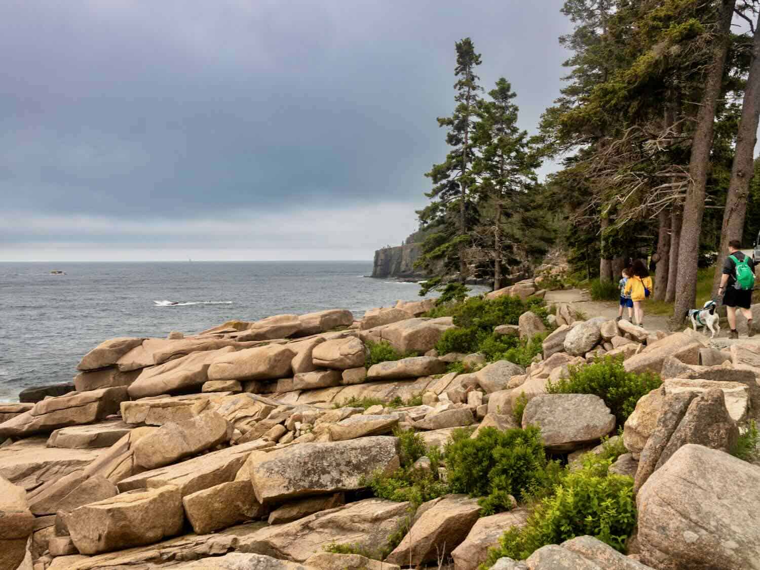 Hikers walk on the Sand Trail Beach next to a rocky coastline in Maine.