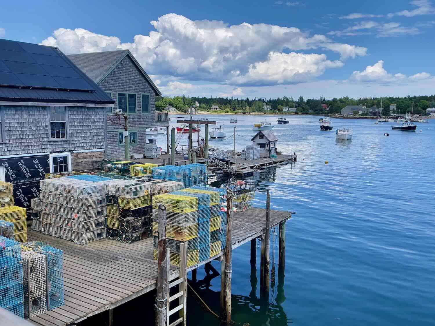 A large cedar building with a dock filled with yellow and blue lobster cages sits at the water in Bernard, Maine.