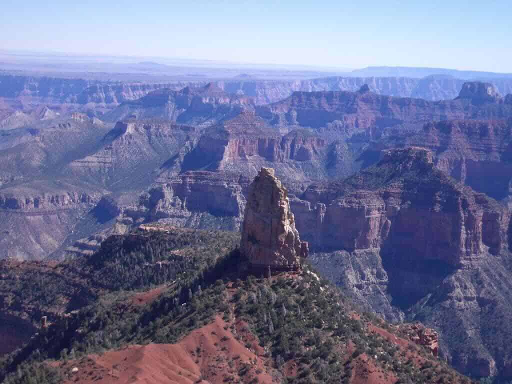 A spire of rock, known as Vishnu Temple, stands on a ridge surrounded by multiple canyon walls in the Grand Canyon.